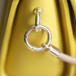 Close-up detail of a yellow leather bag with a shiny silver metal spring ring connector.