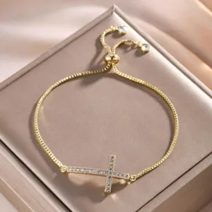 Gedetailleerd close-up van een vergulde armband met dwars geplaatst kruis en zirkonia.
