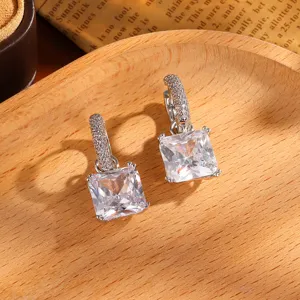 Gedetailleerde close-up van sprankelende vierkante zirkonia oorbellen op een houten dienblad.