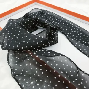 Close-up of black chiffon skinny scarf with white polka dots, elegant neck ribbon accessory.