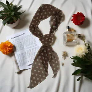 Detail shot of a brown polka dot silk scarf, styled with flowers and perfume on white fabric.
