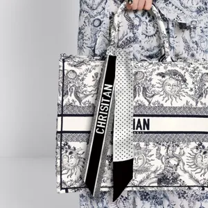 Detailed view of a stylish black and white polka dot silk scarf tied on a tote bag handle.