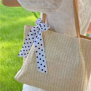 Detail view of a chic straw tote bag decorated with a black and white polka dot ribbon scarf.
