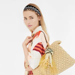 Gros plan d'un bandeau élégant à motifs et d'un sac en paille porté par un mannequin en studio.