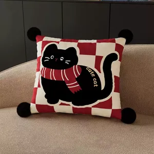 Red checkered throw pillow with cute black cat design and fluffy pom poms for living room.