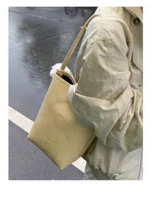 Close-up of minimalist yellow bucket shoulder bag with cute fluffy white charm detail outdoors.