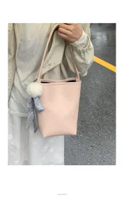 Pink leather bucket bag detail view with cute furry ball and scarf charm, fashion accessory.