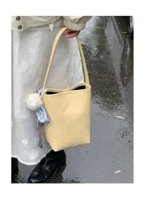 Detailed view of a light yellow bucket bag featuring a chic shoulder strap and cute scarf charm.
