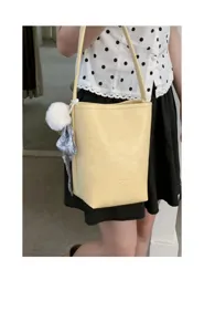 Yellow leather bucket bag detail featuring a cute fluffy plush ball and printed scarf pendant.