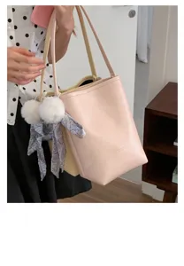 Detailed view of the stylish pink bucket shoulder bag featuring cute pom-pom and scarf charms.