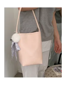 Minimalist pink bucket shoulder bag with cute plush ball and patterned scarf charm detail.