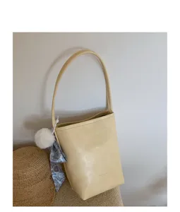 Minimalist yellow bucket bag detail view, featuring chic scarf and pom-pom charm design.