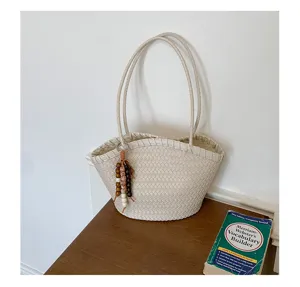 Dettaglio borsa a spalla intrecciata, elegante borsa beige con ciondolo di perle, stile chic.