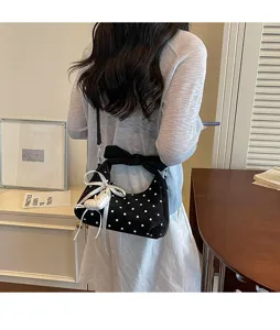 Detail view of black polka dot crescent shoulder bag with cute black bow and white ribbon charm.