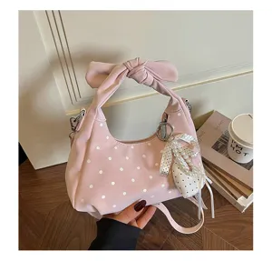 Chic pink polka dot crescent shoulder bag with bow handle and pearl pendant detail.