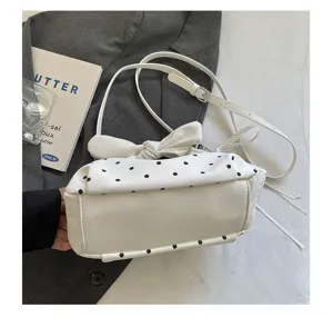 Polka dot handbag detail view, stylish white crescent shoulder bag with bow design.