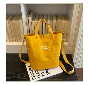 Vue détaillée du sac seau en toile jaune vif avec bandoulière et poche avant pratique.
