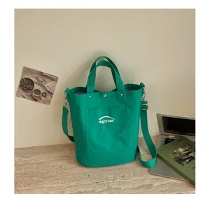 Détail de sac seau en toile verte avec poche avant, poignées solides et sangle d'épaule.
