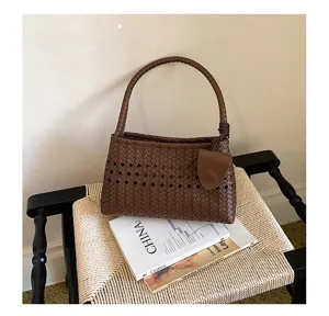Detailed shot of brown woven leather underarm handbag with chic cutout design on chair.