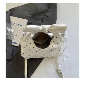 Detailed view of a white polka dot bow handbag detail, crescent shoulder bag design.