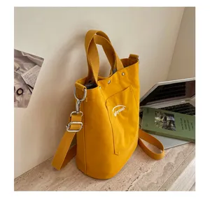 Vue détaillée d'un sac seau en toile jaune avec bandoulière et poche avant pratique.
