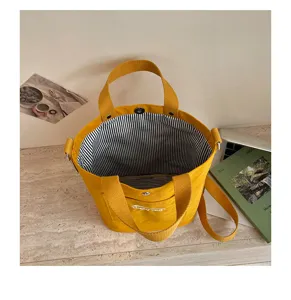 Vue detaillee d'un sac seau bandouliere en toile jaune avec doublure rayee noir et blanc.