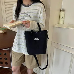 Sac seau décontracté en toile noire avec bandoulière et poche avant pour usage quotidien.
