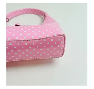 Pink polka dot crescent handbag detail, featuring glossy patent leather and fine neat stitching.