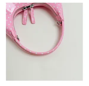 Pink polka dot crescent handbag, stylish patent leather shoulder bag with zipper detail.