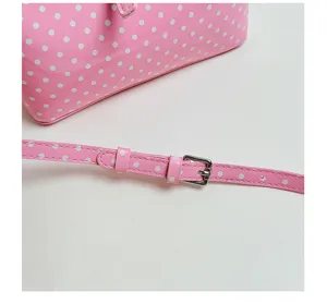 Pink polka dot crossbody bag detail shot, glossy PU leather material with adjustable thin strap.