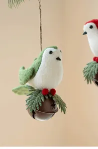 Close-up detail of felt bird Christmas ornament with metal bell, pine needles, and berries.