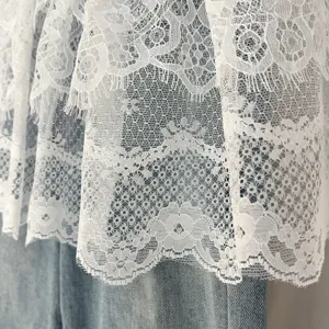 Vista detallada de exquisito tejido de encaje blanco con patrones florales superpuestos.