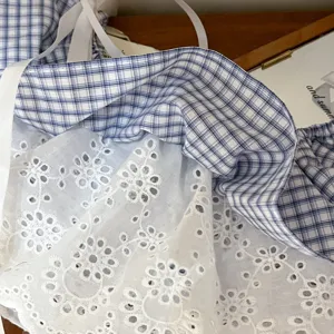 Detailed view of blue and white plaid fabric with white floral lace embroidery and fabric straps.