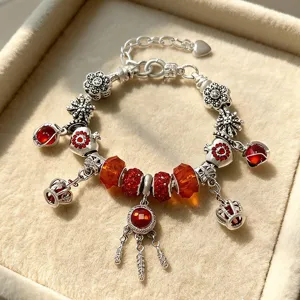 Detailaufnahme eines Silber-Charm-Armbands mit funkelnden roten Kristallperlen und Anhängern.