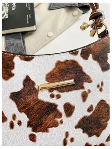 Vista dettagliata della borsa a spalla con stampa mucca marrone e bianca e dettagli dorati.