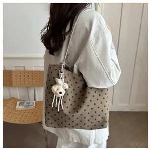 Dettaglio di una borsa shopper in tela a pois marroni con ciondolo in peluche morbido.
