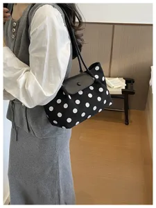 Detail view of the black canvas shoulder bag featuring classic white polka dots and a sleek flap.
