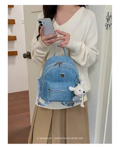Close-up detail of the stylish denim backpack showing texture and plush toy keychain decoration.