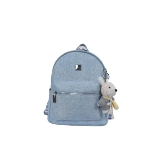 Close-up of light blue denim backpack with sparkling rhinestones and cute knitted bear pendant.