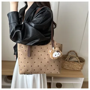 Vista dettagliata della borsa tote marrone a pois con logo metallico e ciondolo.