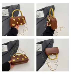 Detailed view of brown hard-shell evening clutch bag with gold studs and metallic handle.