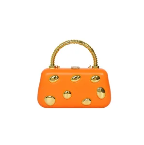 Close-up of orange hard shell clutch bag with shiny gold pebble studs and metallic handle.