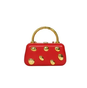 Red hard-shell clutch handbag featuring a golden ribbed handle and shiny gold pebble studs.