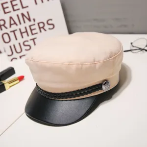 Detailed view of beige baker boy hat with black leather brim and braided strap accent.