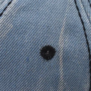 Gros plan détaillé du tissu en denim bleu de la casquette avec couture noire et œillet.