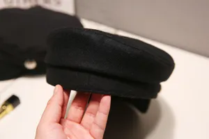 Black newsboy cap detail shot, showing the classic brim and structured wool fabric texture.