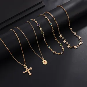 Ensemble de colliers dorés superposés avec pendentif croix et strass colorés.