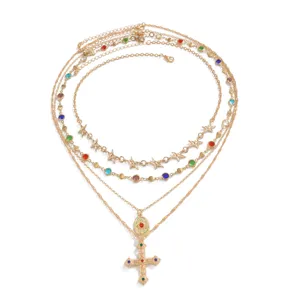 Ensemble de collier doré multicouche avec pendentif croix et breloques en pierres précieuses.