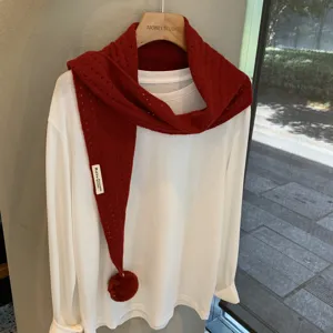 Detailed shot of red knit triangular scarf with hollow design and cute pom-pom decor.