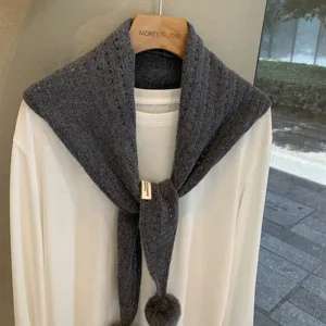Grey knitted triangle scarf shawl with pom pom hollow out design layered over white shirt.